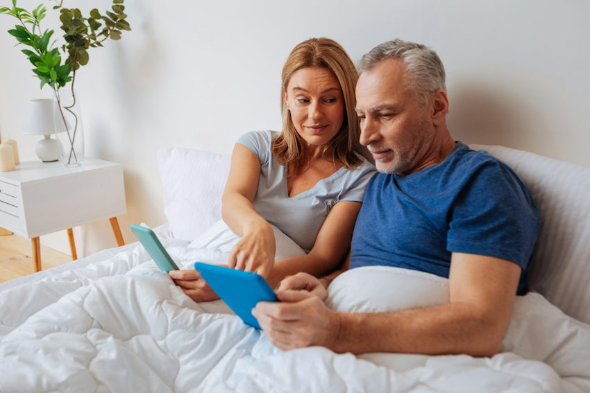 Gen X Couple looks at ipads snuggled in bed