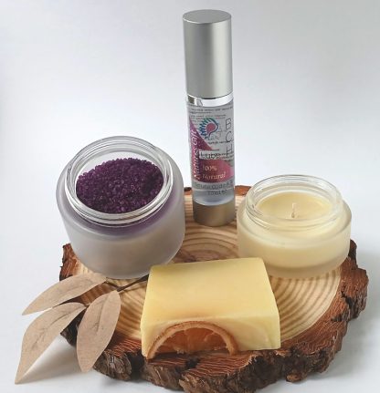 Bath Salts in a frosted Glass Jar bottle of BCH Naturals glide oil, soap and Candle on a slice of Wood with green leaves