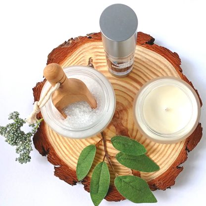 a view from the top - Bath Salts in a frosted Glass Jar bottle of BCH Naturals Lube and Candle on a slice of Wood with green leaves