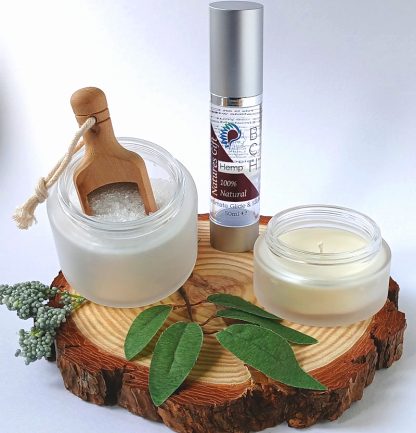 Bath Salts in a frosted Glass Jar bottle of BCH Naturals Lube and Candle on a slice of Wood with green leaves