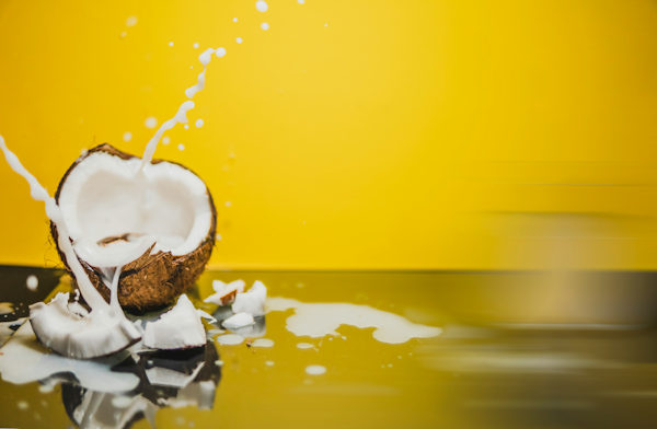 Coconut smashed with milk flying out of it on a bright background