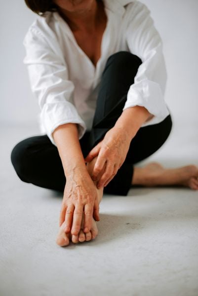 A middle aged lady sitting on floor in trousers with a shirt on and no shoes (you can tell she is middles aged by her hands)