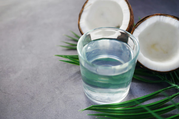A fresh coconut in two halves with a small glass of coconut water with slim green leaves