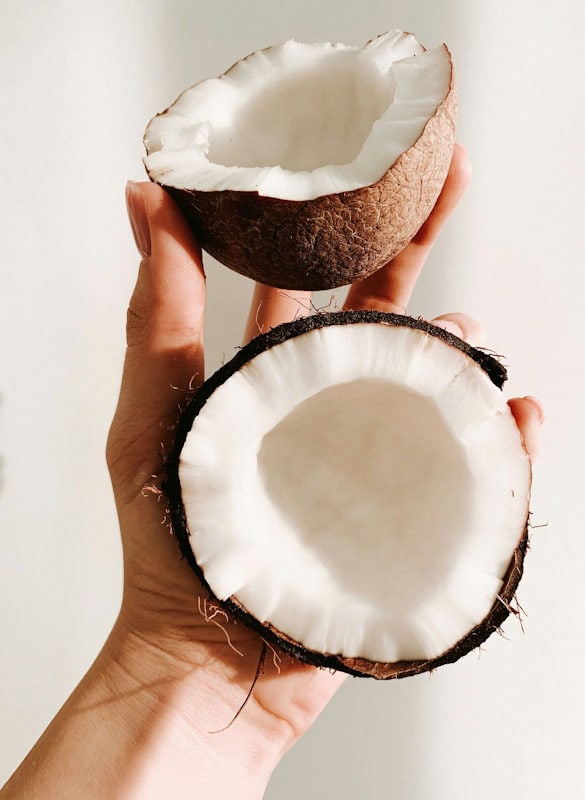 A hand holding two fresh coconut halves