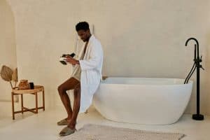 Midlife man in a white robe relaxing beside a modern bathtub, embracing calm and self-care with natural lubricant for men | Natural oils – BCH Naturals.