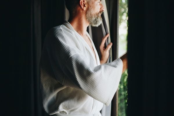 Middle aged Man looking out of a drawn curtain. relaxing after intimacy.