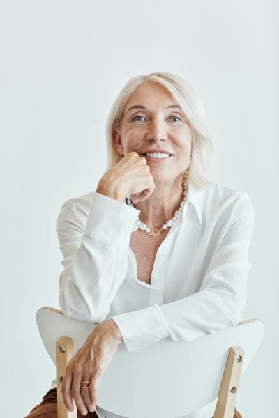 Confident woman sat on a backwards white chair in a white blouse