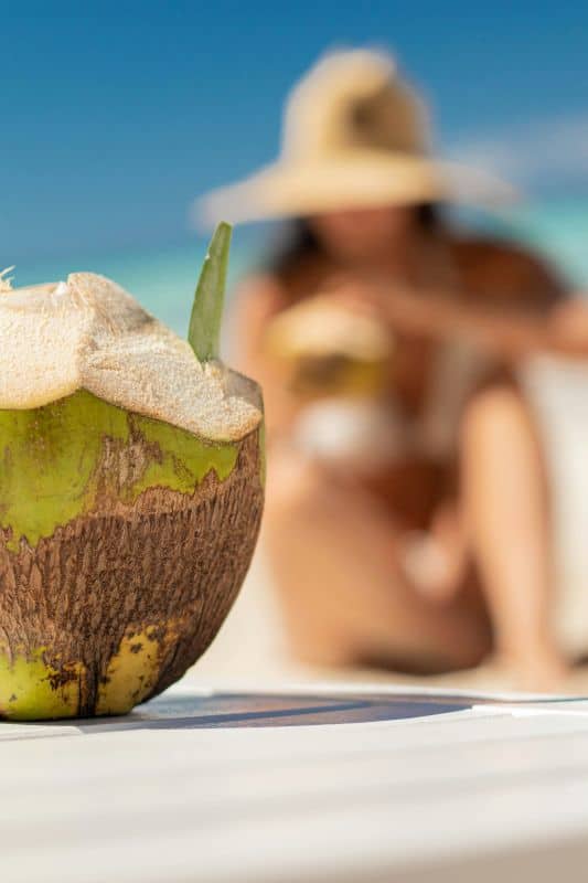 lady on a beach in a white bikini with a fresh cut open coconut