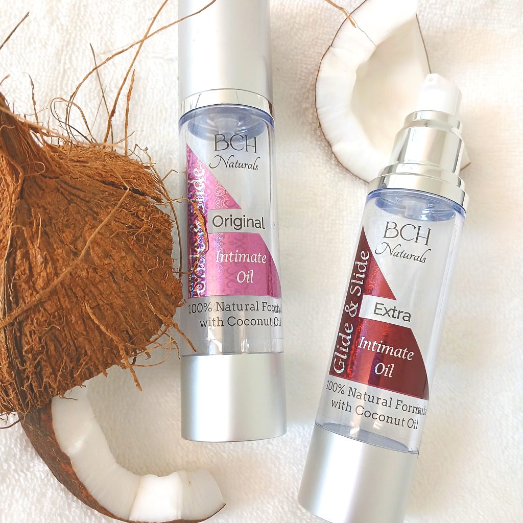 Original & Extra Coconut Oil Intimate Oil on a white towel surrounded by real coconuts